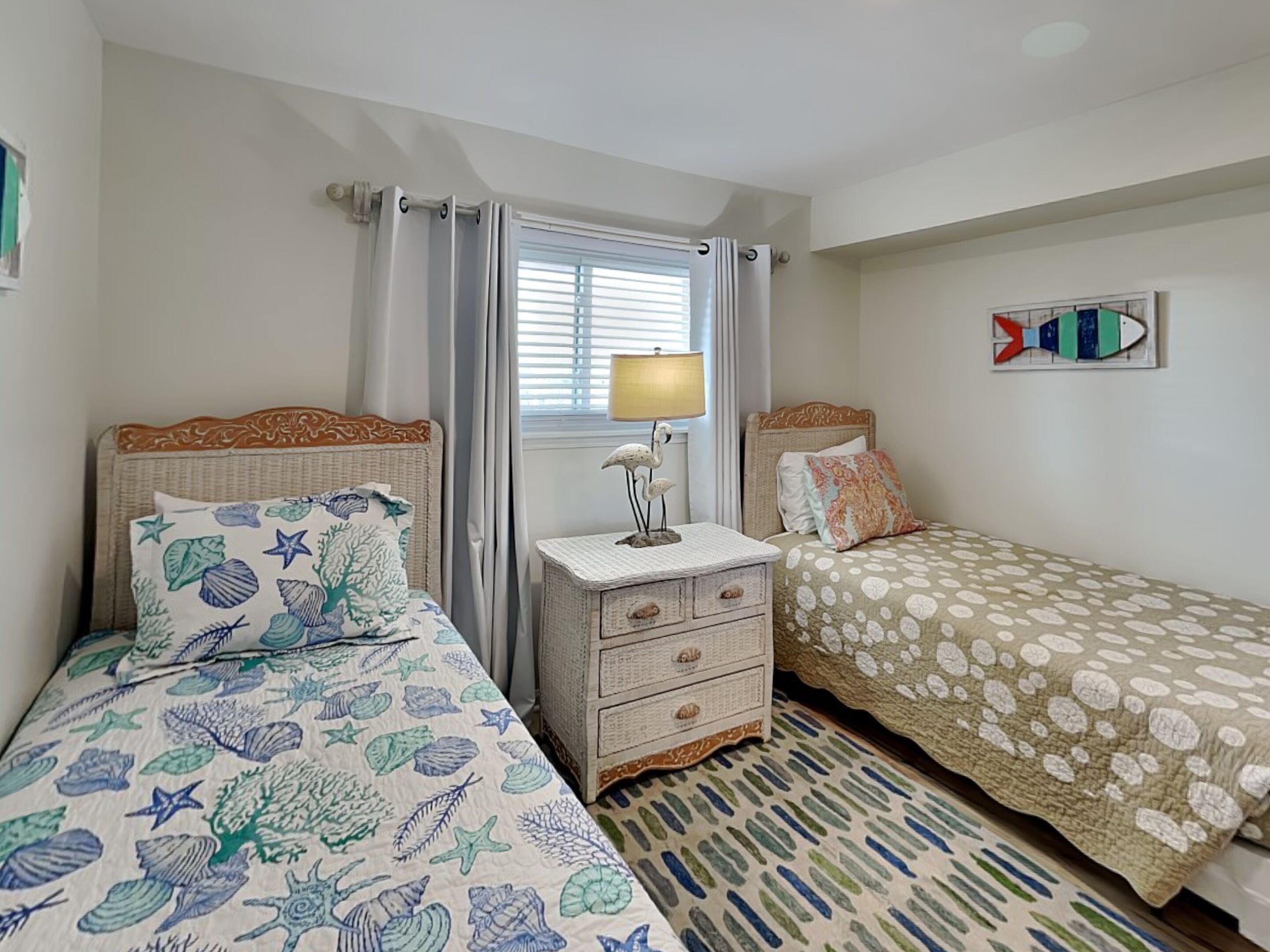 A bedroom with two beds, a nightstand, a lamp, and a window with curtains.