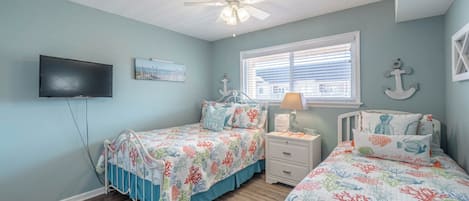A bedroom with two beds, a ceiling fan, a TV, and a window with blinds.