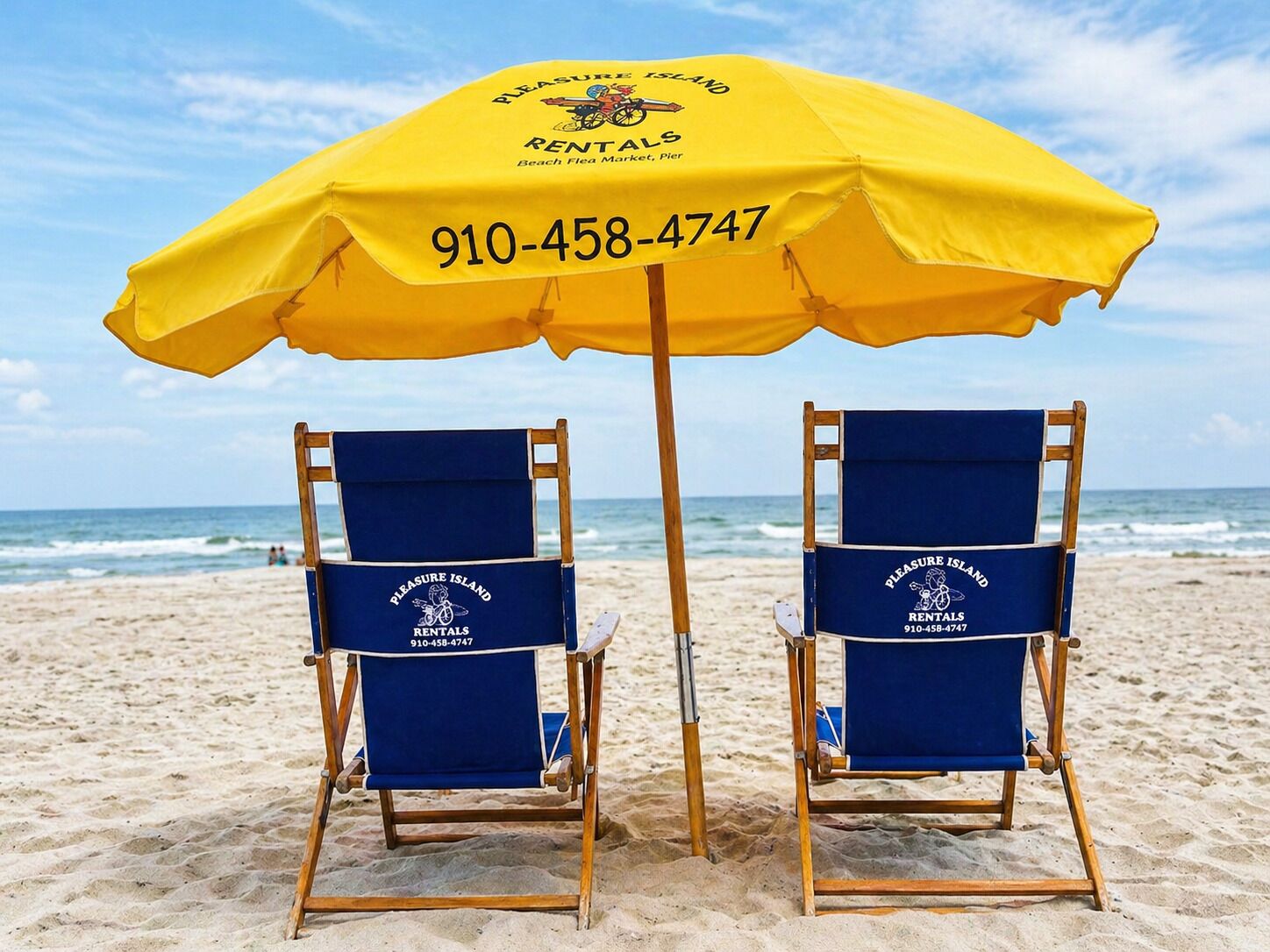 Dos sillas de playa bajo un paraguas amarillo con la marca 'Pleasure Island Rentals' y número de contacto.