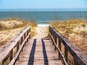 A wooden boardwalk leading to a beach with sand and grass on either side. - Sand Pebbles by Carolina Retreats (Carolina Beach)