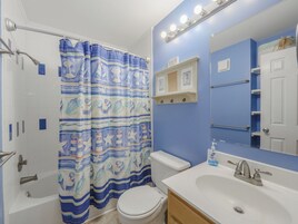 A bathroom with a shower curtain, toilet, sink, and mirror.