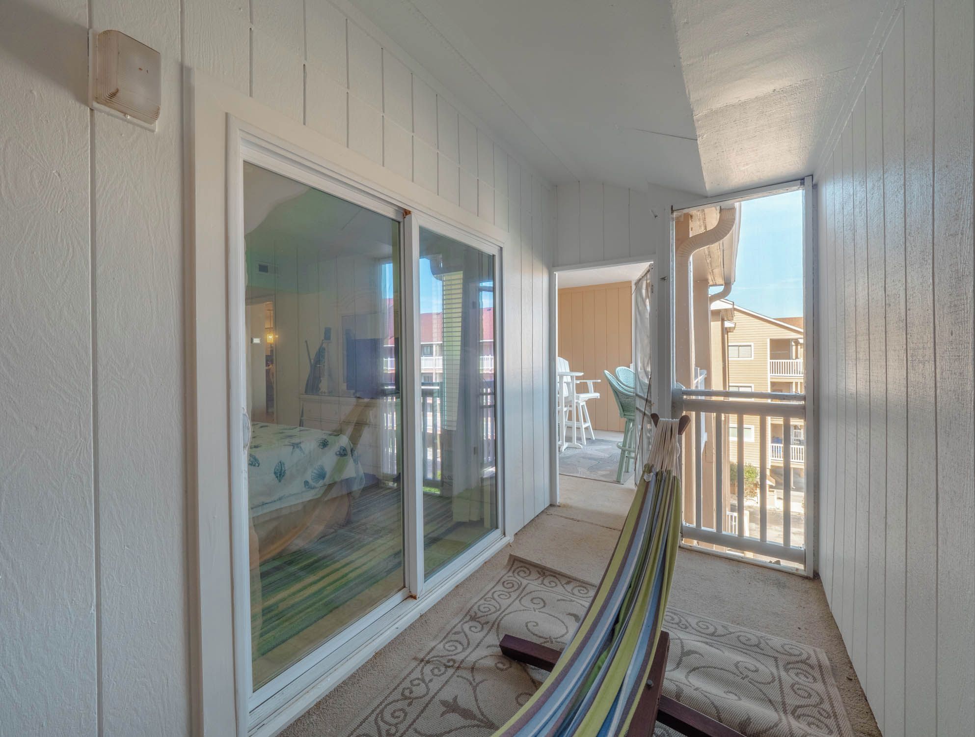 Ein Balkon mit einer Hängematte, Glastüren und Blick ins Freie.
