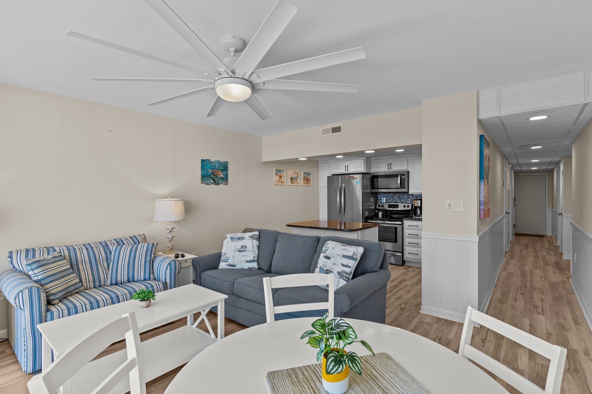 A modern living room with a grey sofa, a white dining table, and a ceiling fan.