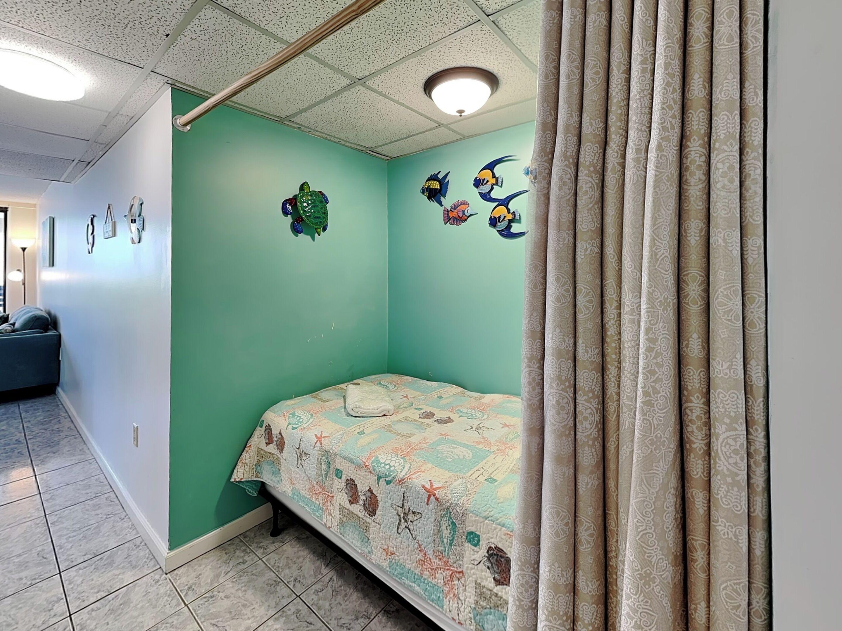 Een kamer met turquoise wanden, een bed met een geborduurd sprei, decoratieve wandkunst en een gordijn.
