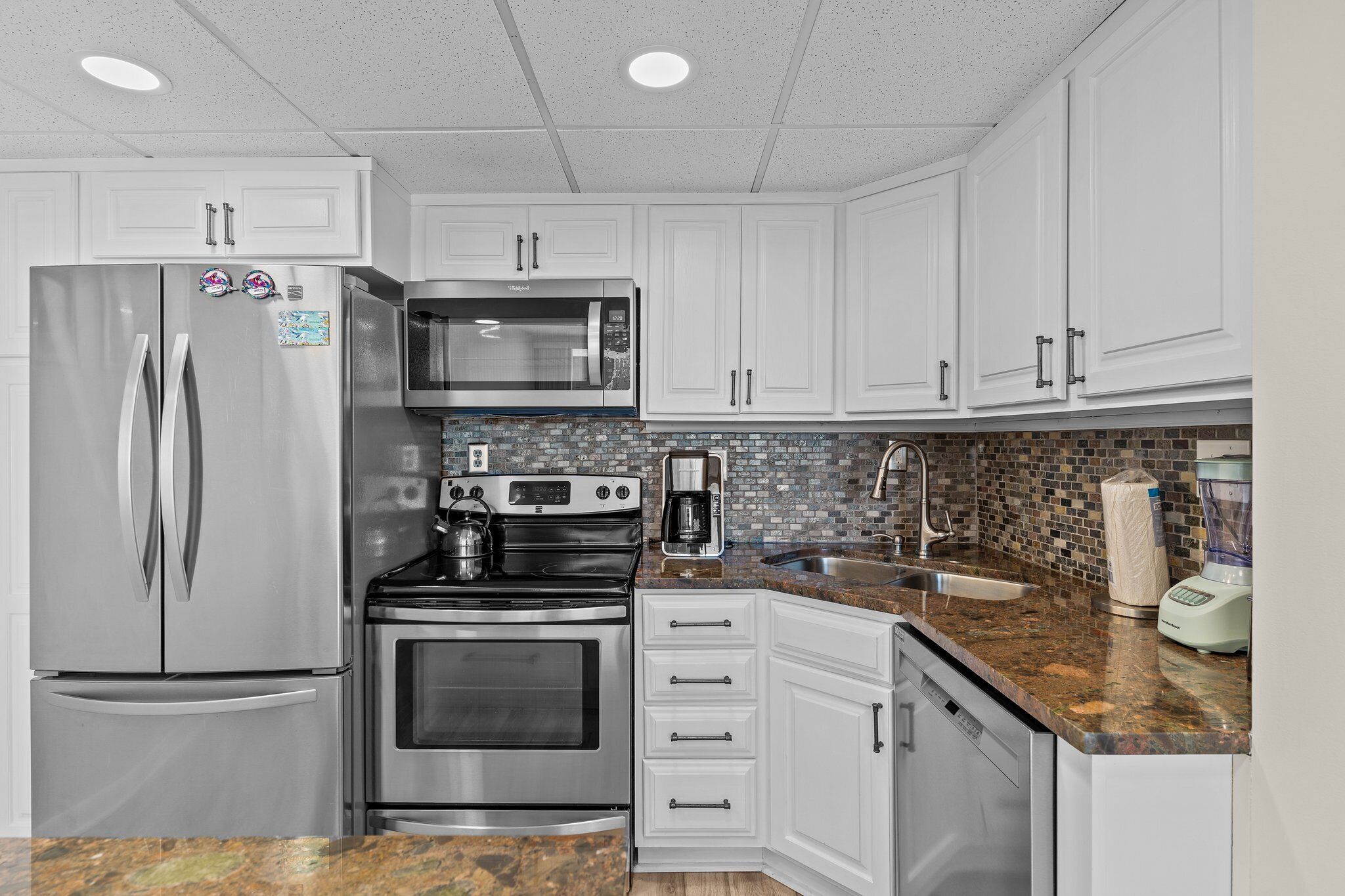 A kitchen with white cabinets, stainless steel appliances, a microwave, stove, and a coffee maker.