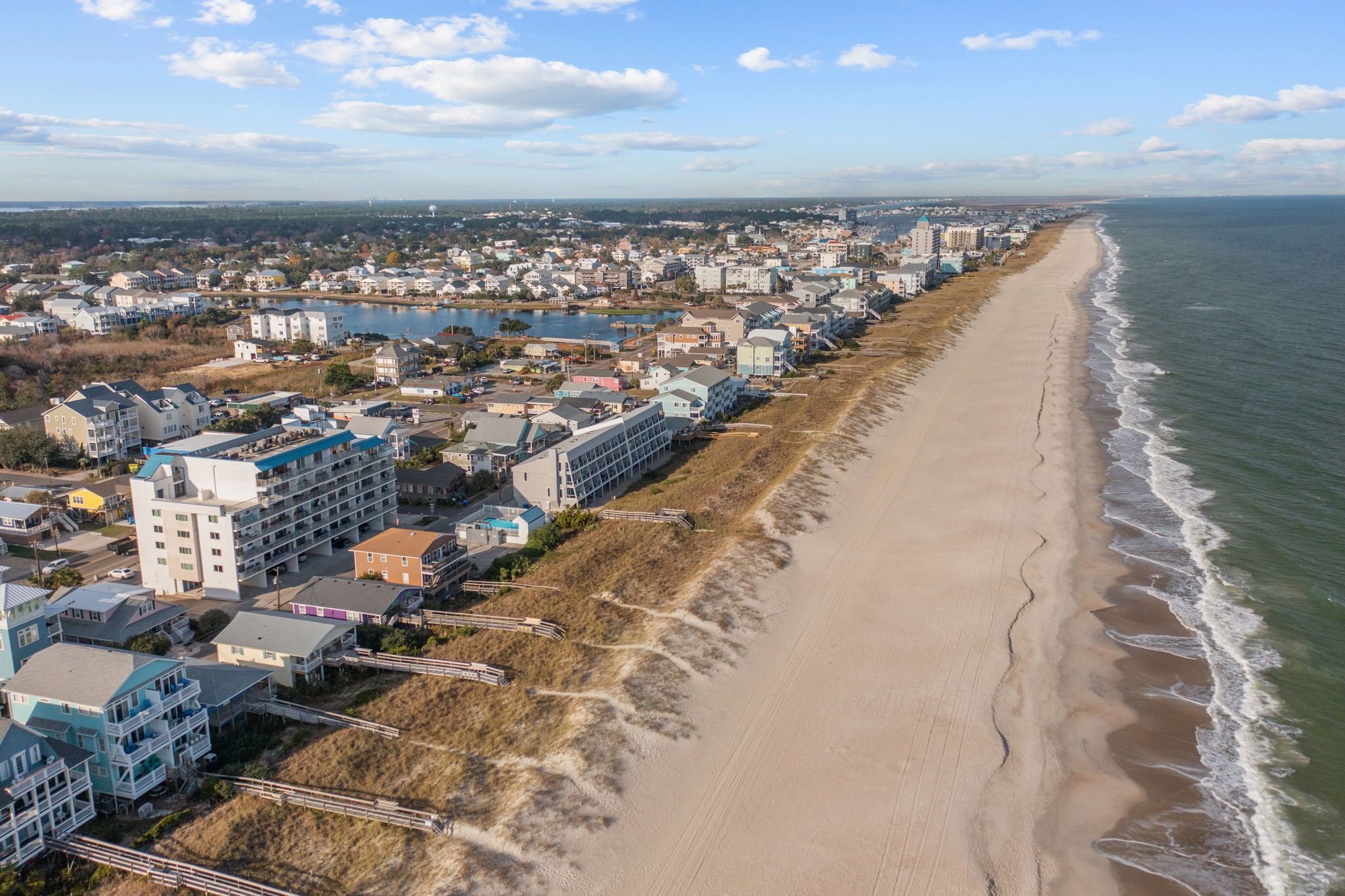 A coastal town with a long sandy beach, buildings along the shore, and a body of water in the background.
