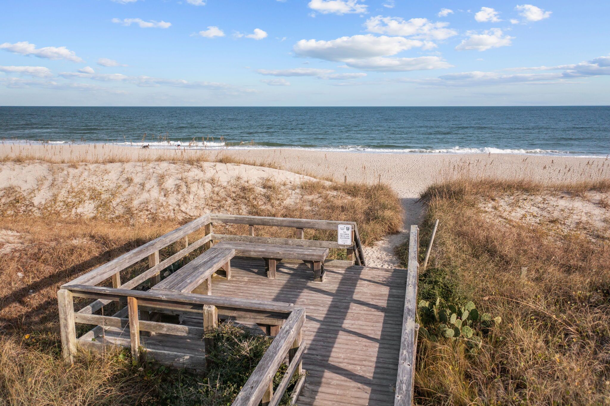 Une promenade en bois qui mène à une plage de sable et offre une vue sur l’océan.