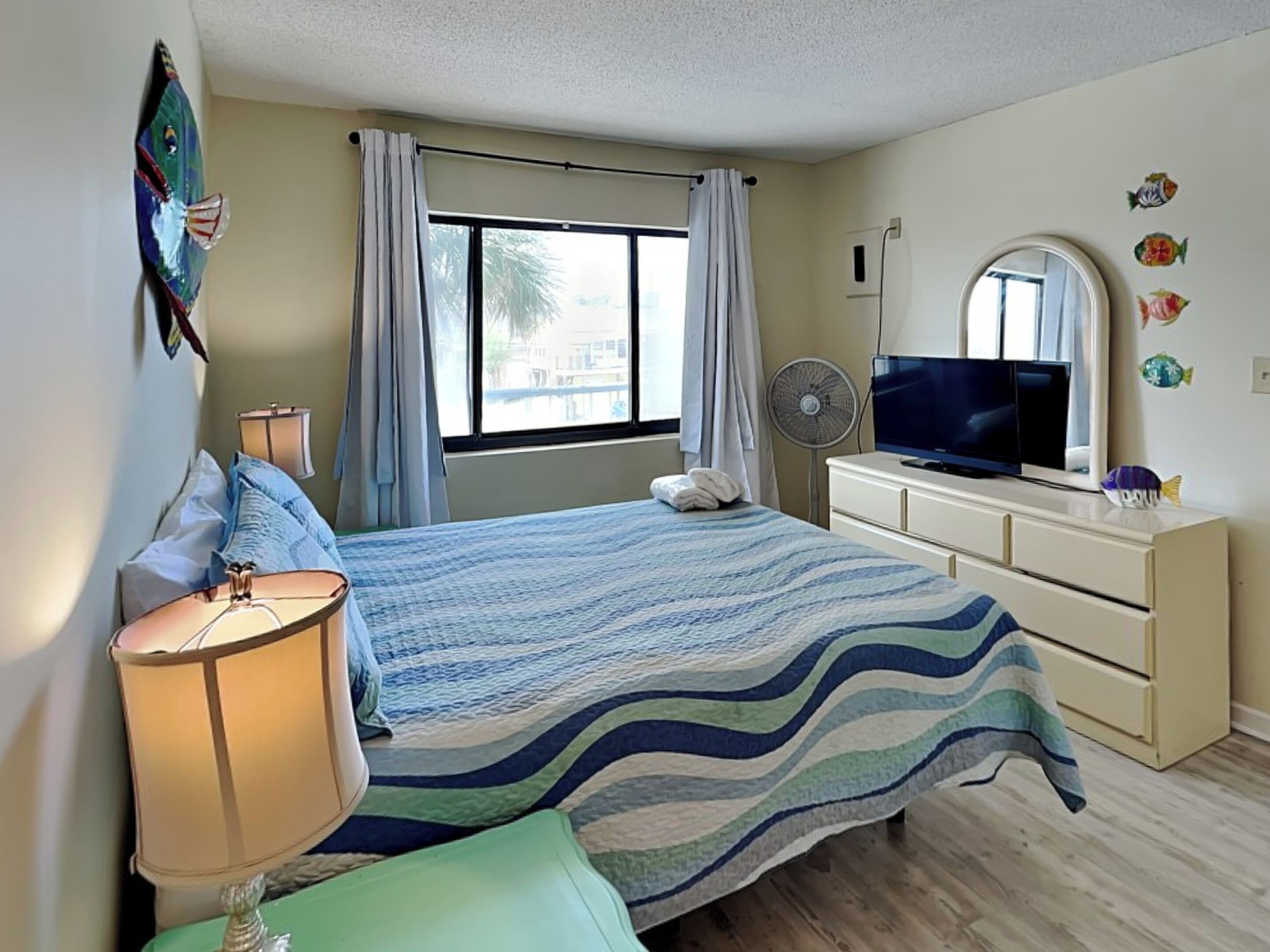 A bedroom with a bed, a TV, a dresser, and a window with curtains.
