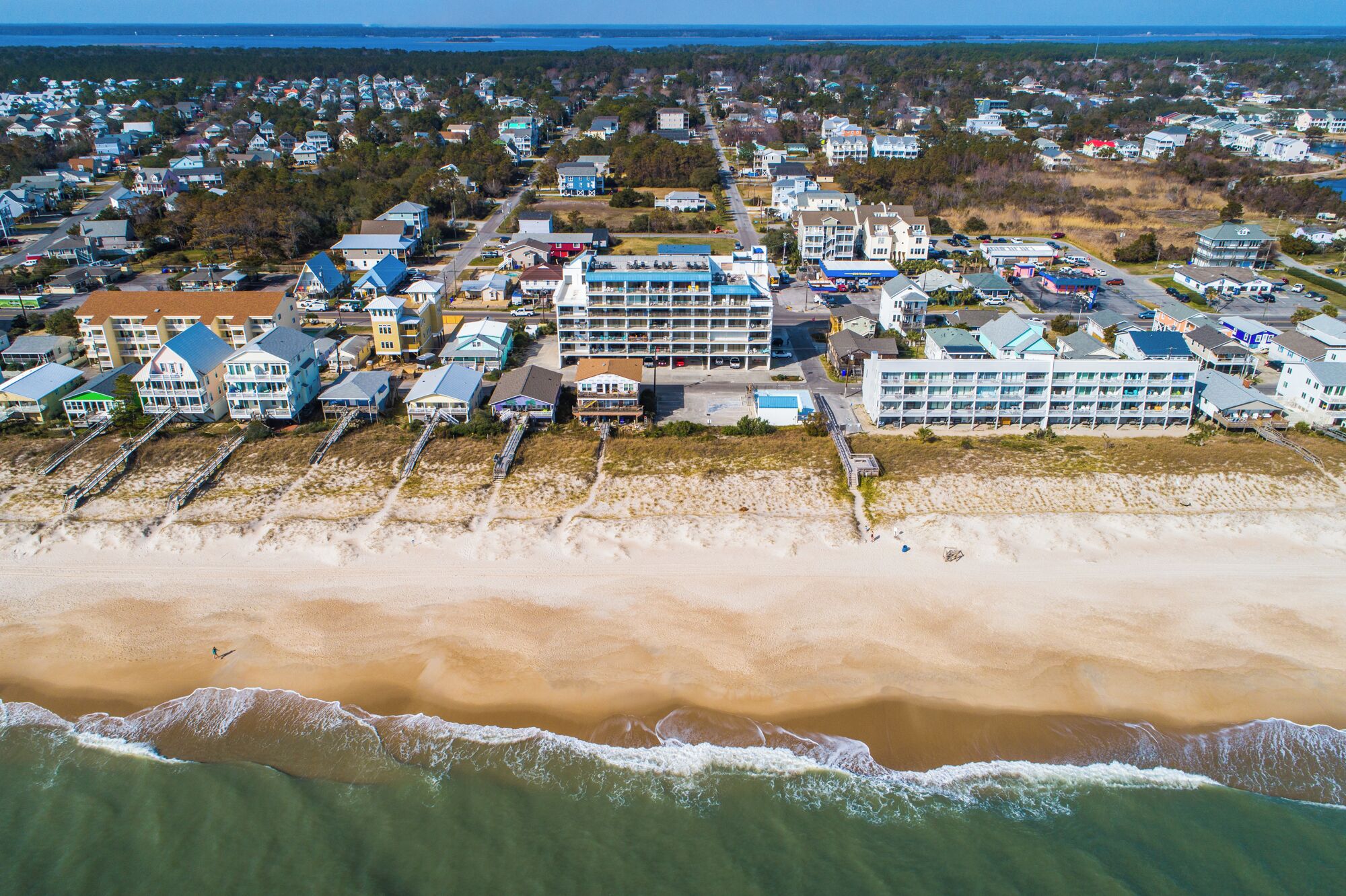 An aerial view of a coastal town with beachfront properties, including multi-story buildings and a beach with a walking path.