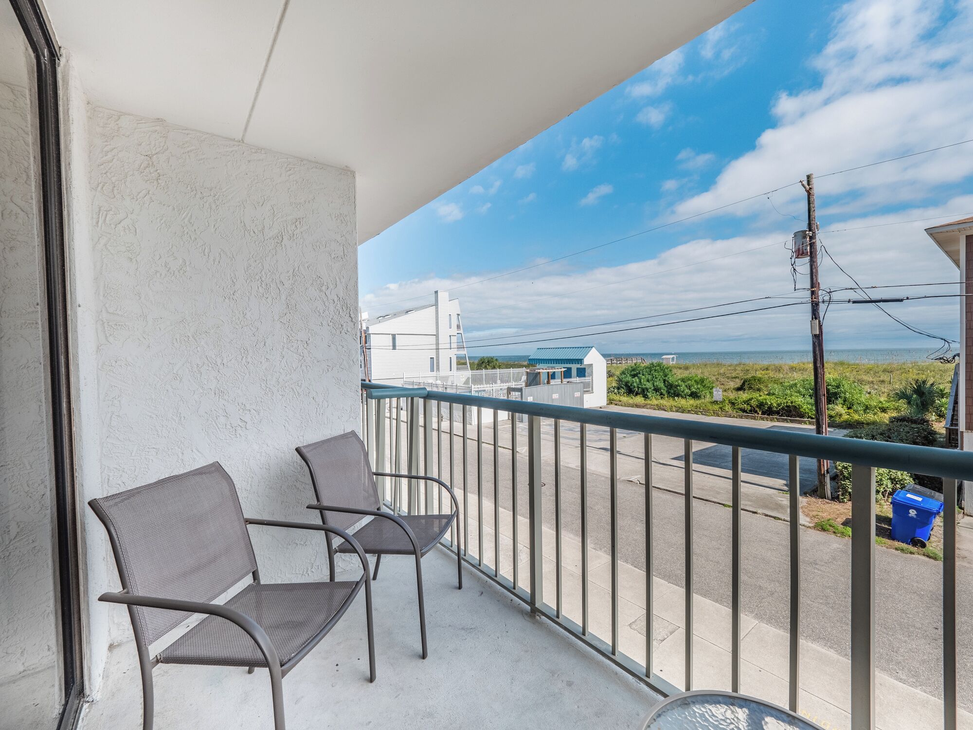 A balcony with two chairs, a railing, and a view of the sea and buildings.