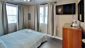 A bedroom with a bed, a ceiling fan, a TV, and a wooden dresser. - CB Seabee #2 by Carolina Retreats (Carolina Beach)