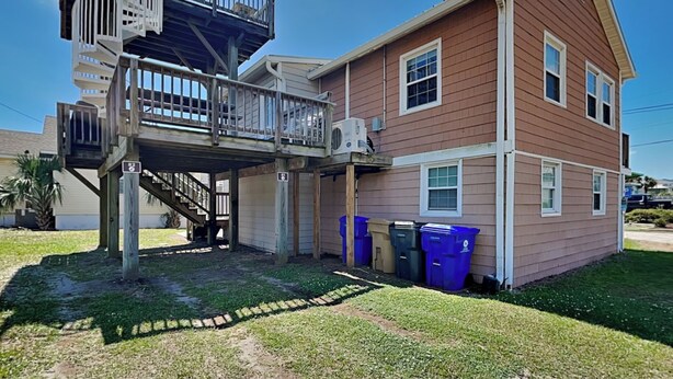 A two-story house with a balcony and a staircase leading to an upper level. There are two trash bins outside the house. - CB Seabee #2 by Carolina Retreats (Carolina Beach)