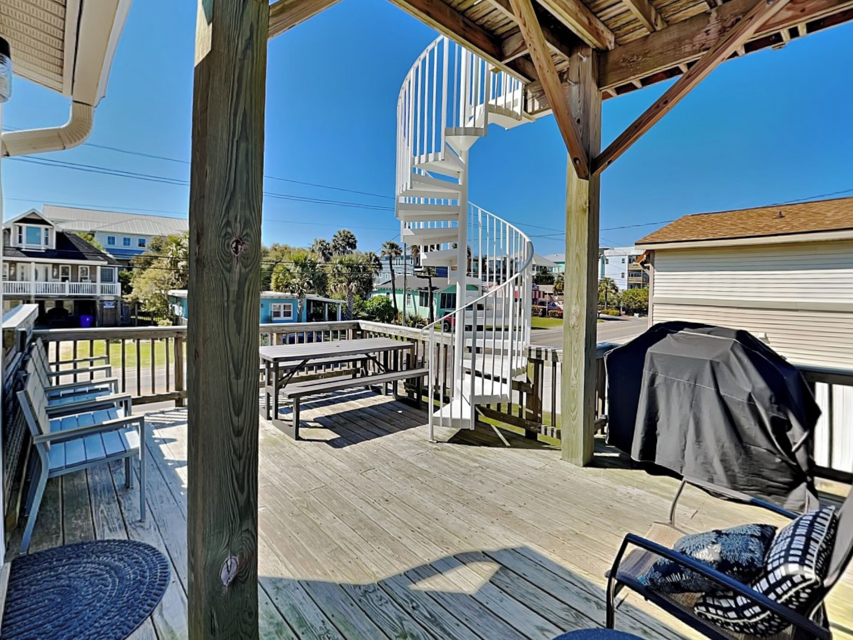 A wooden deck with a covered seating area, a spiral staircase, and a view of surrounding buildings.