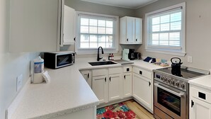 A modern kitchen with white cabinets, a microwave, a kettle, and a coffee maker. - CB Seabee #2 by Carolina Retreats (Carolina Beach)