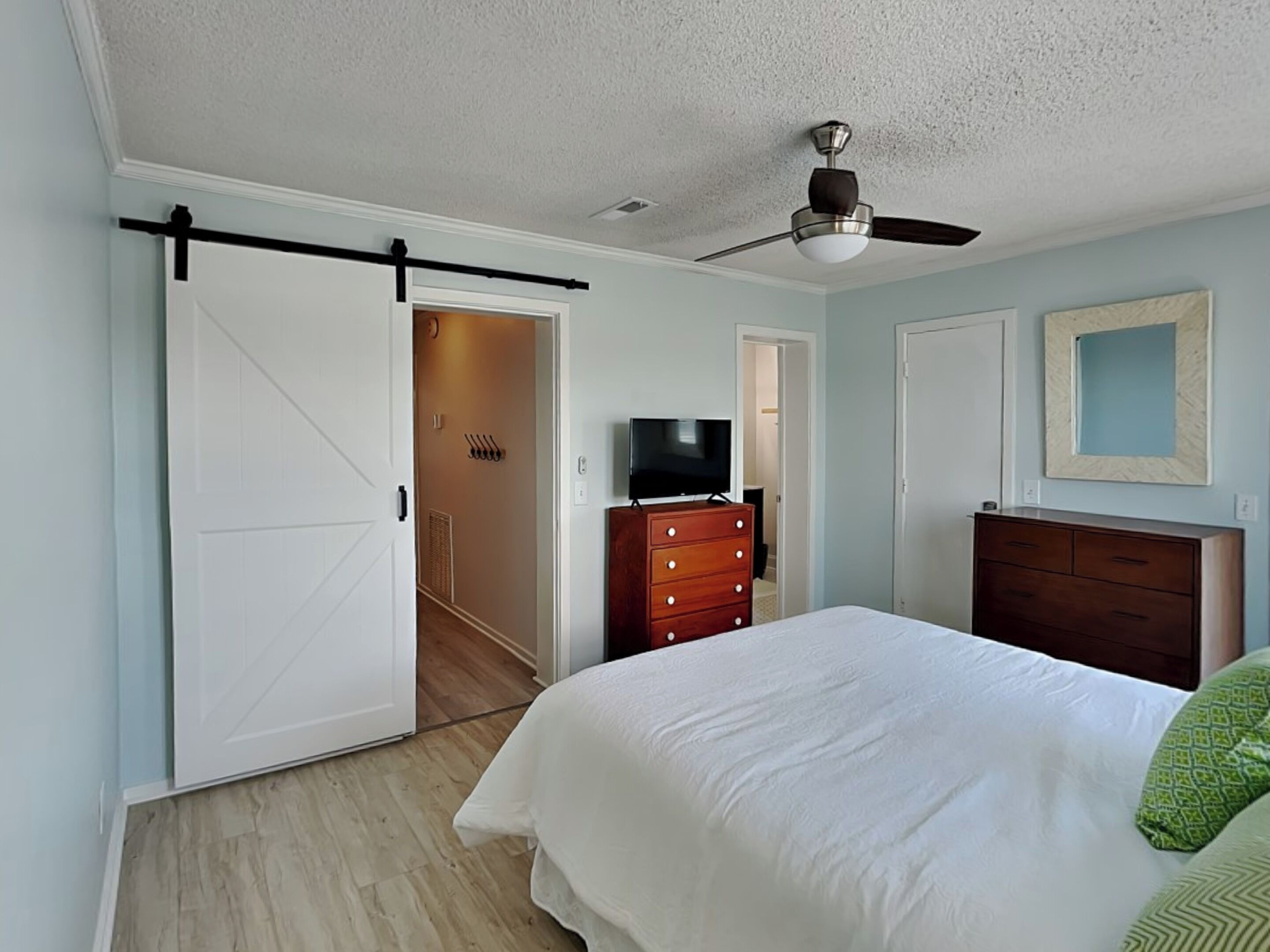 A bedroom with a bed, a dresser, a television, and a ceiling fan.