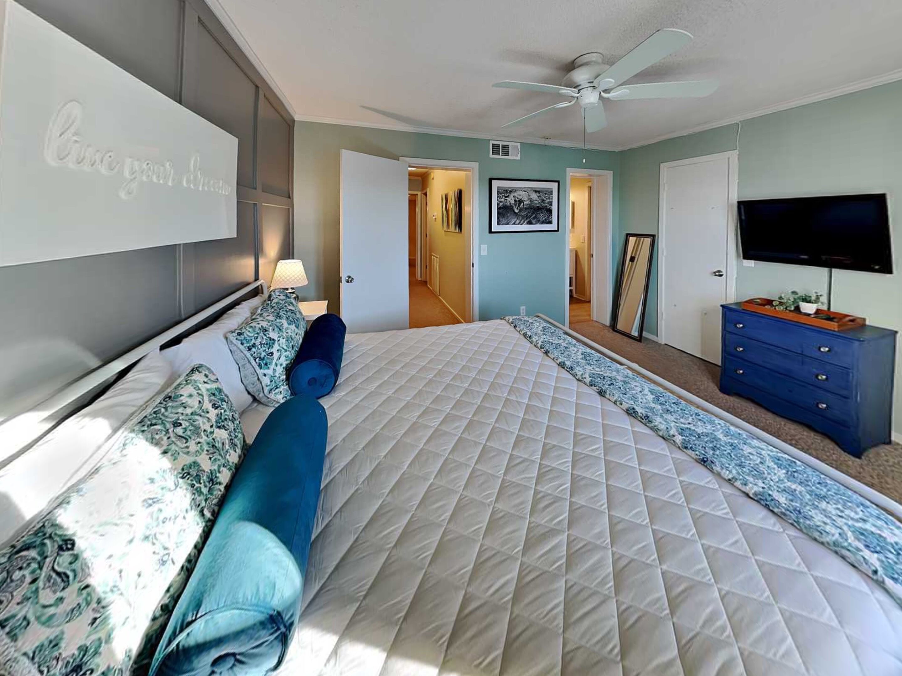 Une chambre avec un grand lit, un ventilateur de plafond, une télévision et une commode.