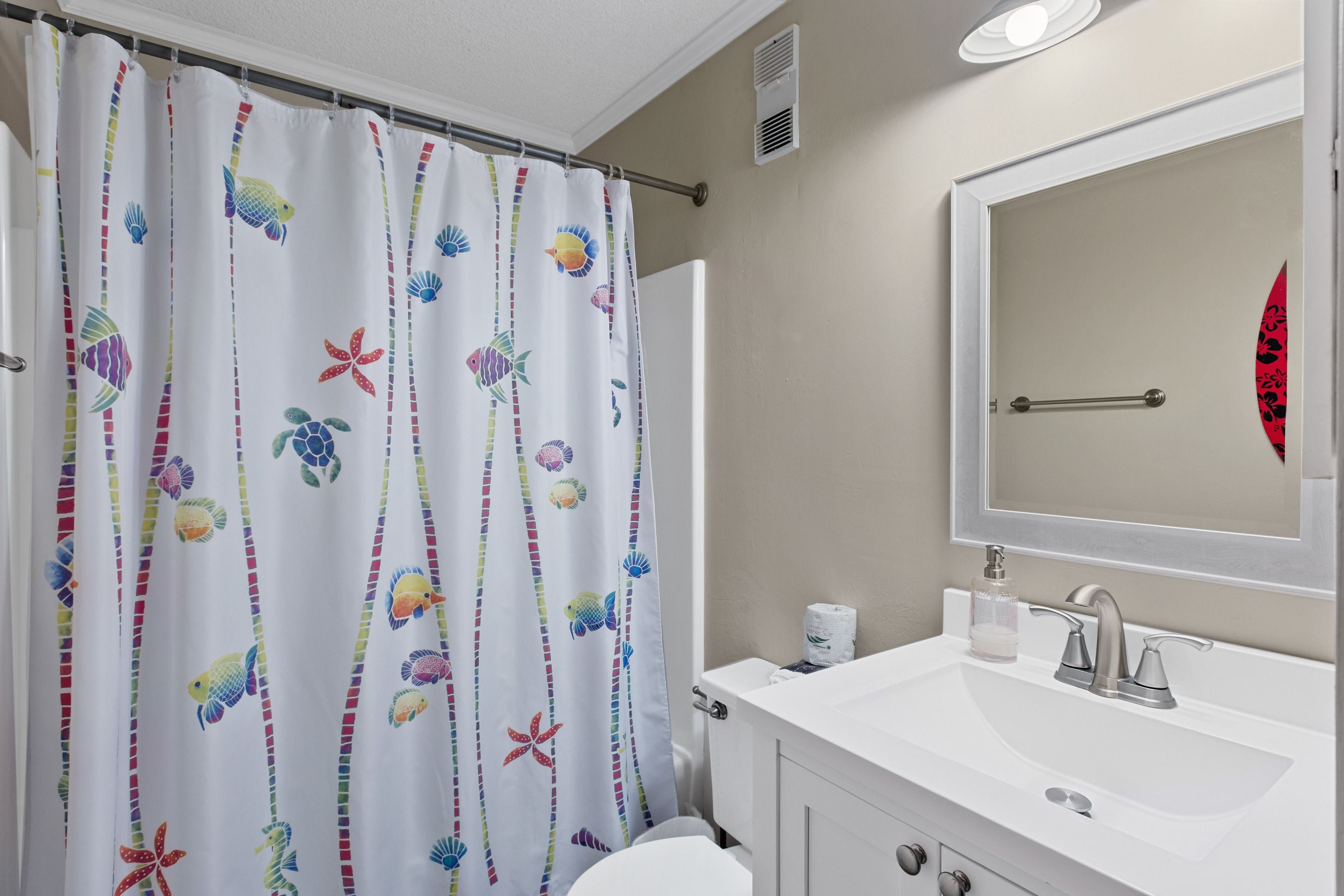 A bathroom with a white sink, mirror, and a shower curtain with a fish and starfish pattern.