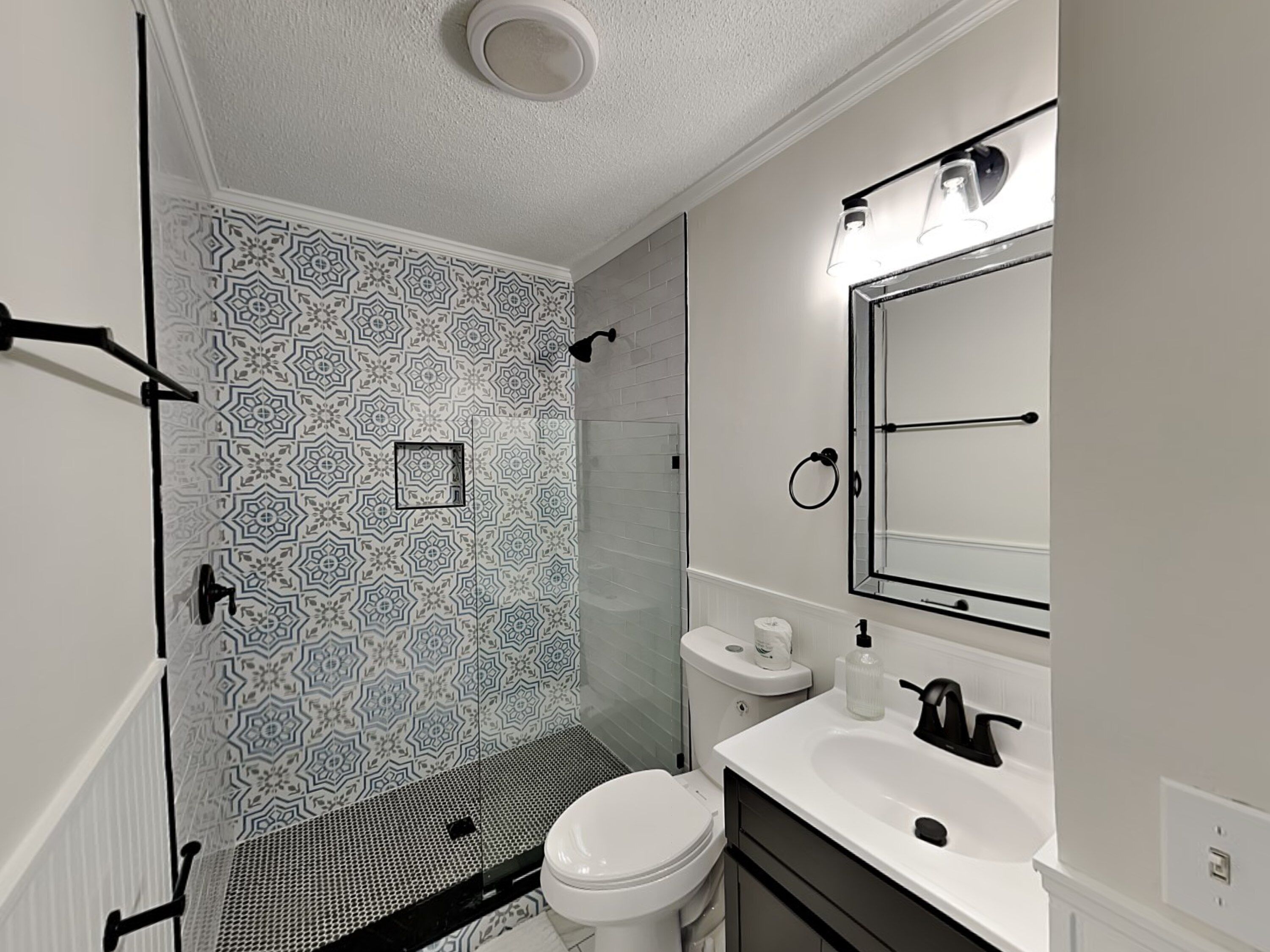 A bathroom with patterned tiles, a toilet, a sink, and a mirror.