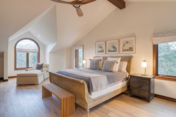 A bedroom with a large bed, a bench, a nightstand, and a ceiling fan.