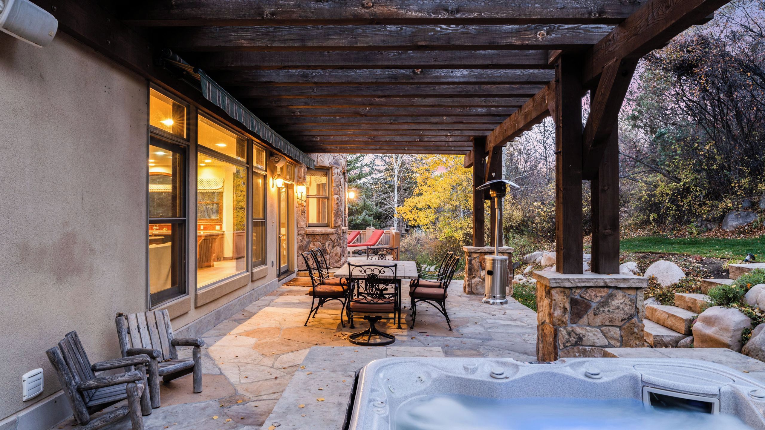 Un patio cubierto con suelo de piedra, jacuzzi, mobiliario de exterior y una pared de piedra.
