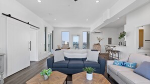A modern living room with a sofa, coffee table, and a dining area. - Boardwalk Pent House by Carolina Retreats (Carolina Beach)