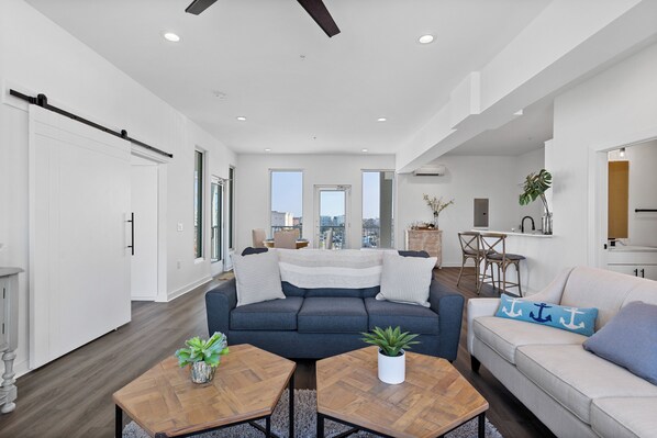A modern living room with a sofa, coffee table, and a dining area. - Boardwalk Pent House by Carolina Retreats (Carolina Beach)