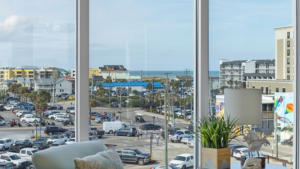 A view from a window overlooking a busy street with buildings and a beach in the background. - Boardwalk Pent House by Carolina Retreats (Carolina Beach)