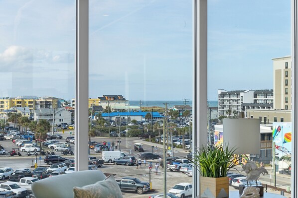 A view from a window overlooking a busy street with buildings and a beach in the background. - Boardwalk Pent House by Carolina Retreats (Carolina Beach)