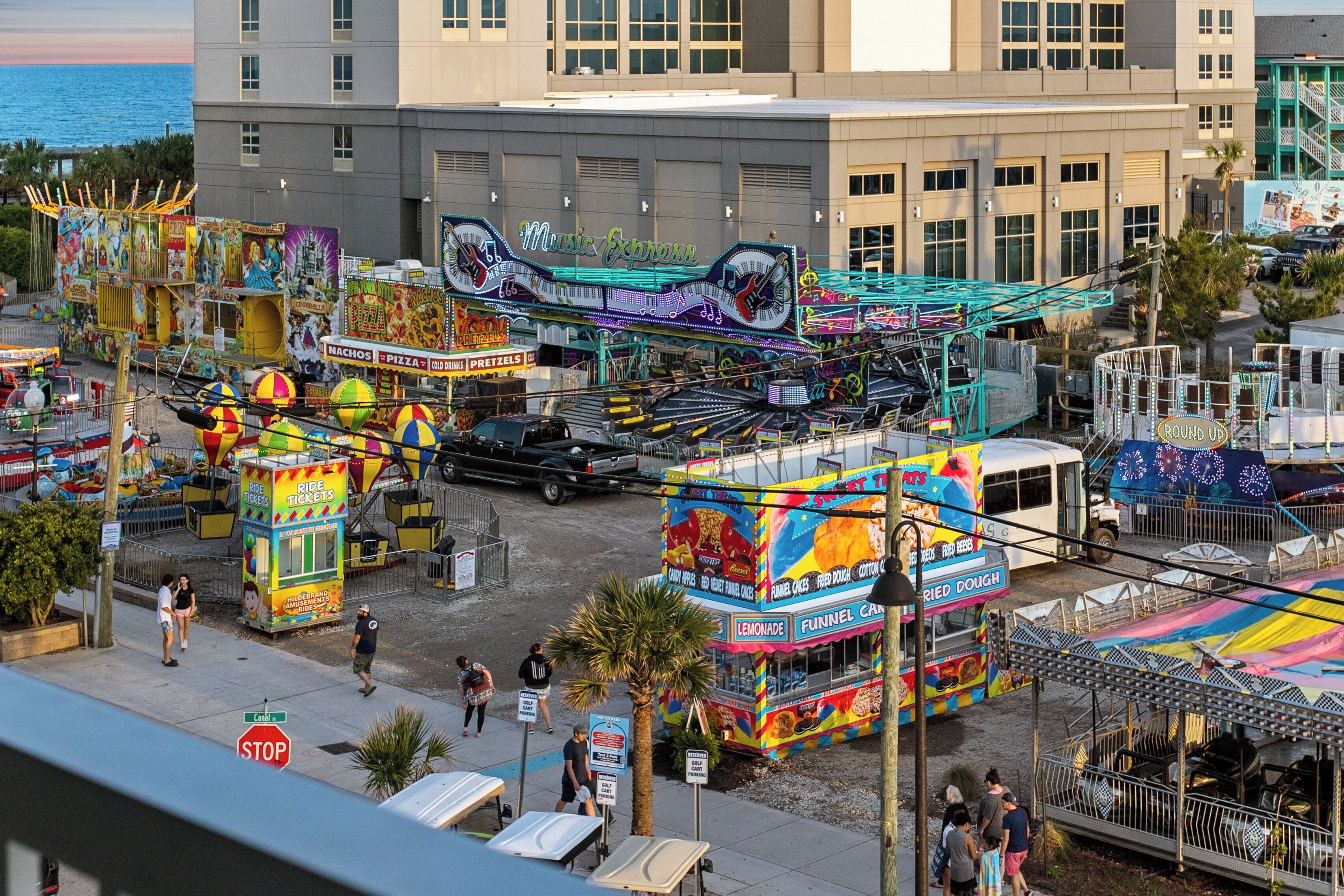A vibrant amusement park with various rides and food stalls, including a Ferris wheel and a ride ticket booth.