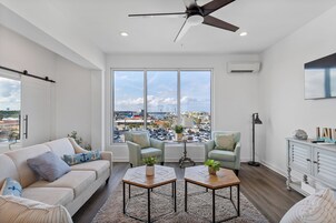A spacious living room with a large window, a ceiling fan, and a view of the cityscape.