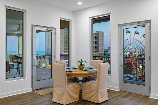A dining area with a round table, four chairs, and a view of a Ferris wheel through a glass door. - Boardwalk Pent House by Carolina Retreats (Carolina Beach)