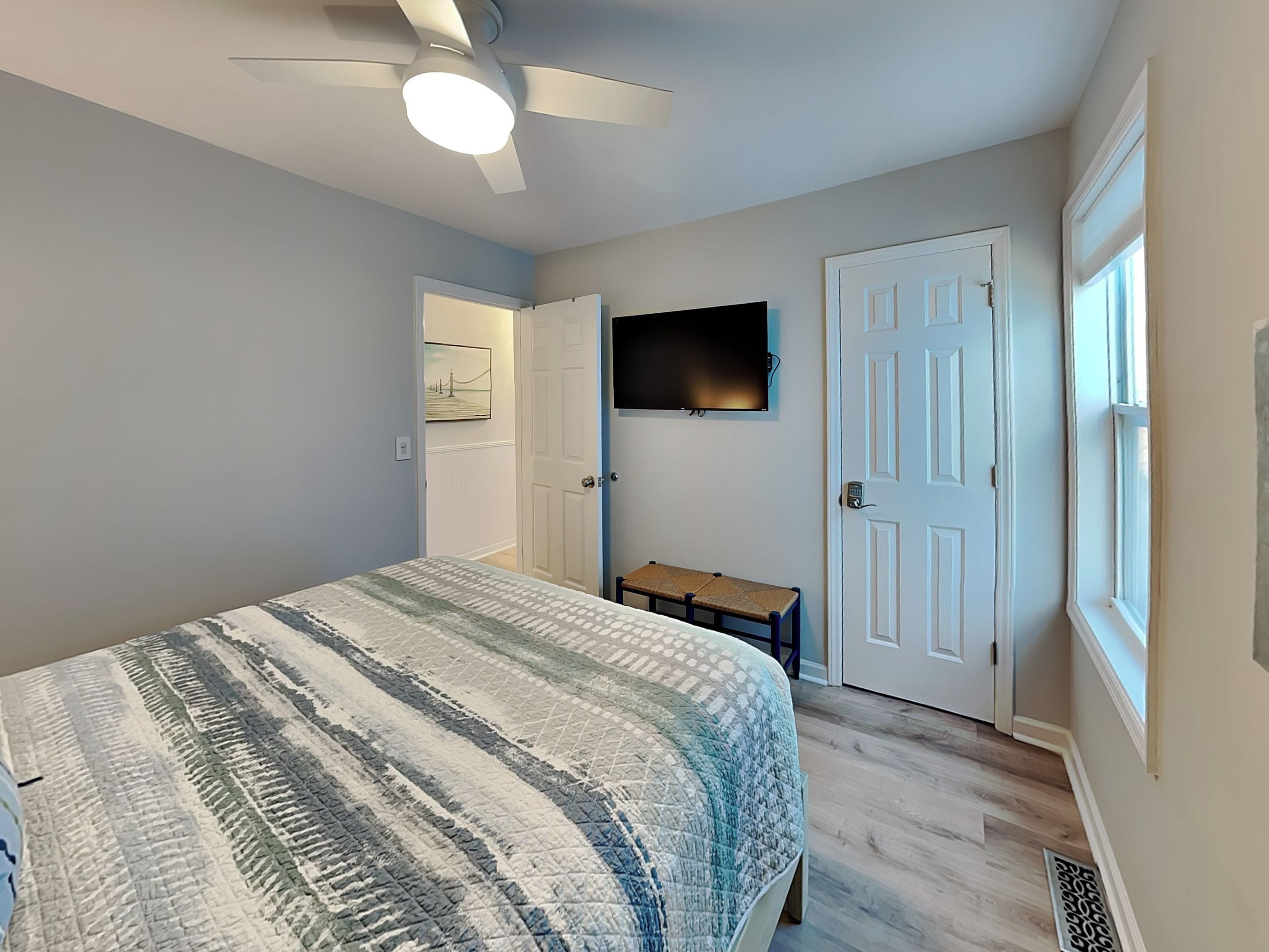 Una camera da letto con un letto, una ventola a soffitto, una TV montata a parete e una porta.