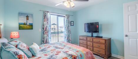 A bedroom with a bed, a dresser, a television, a ceiling fan, and a painting of a lighthouse.