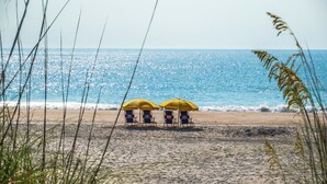 En strand med två gula parasoller och två strandstolar som är vända mot havet.