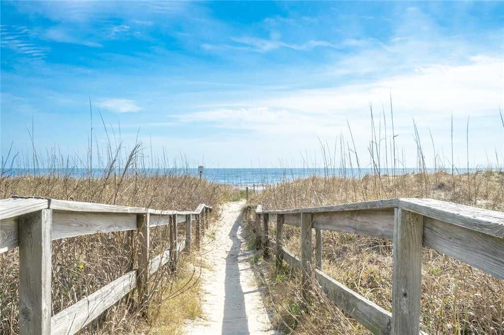 Ein hölzerner Steg führt zu einem Strand unter blauem Himmel.