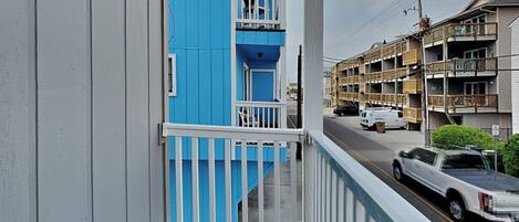 A balcony with a view of a street, a blue building, and a white truck parked on the road.
