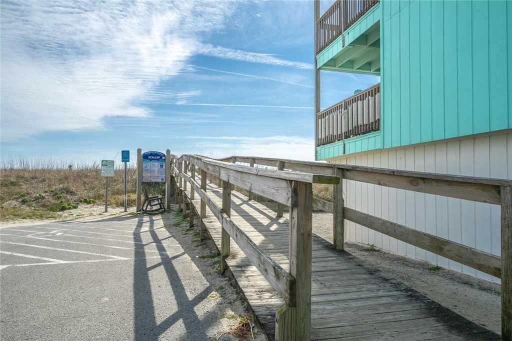 A wooden boardwalk leading to a building with a teal facade and balconies.