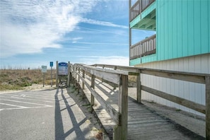 A wooden boardwalk leading to a building with a teal facade and balconies. - Winds by Carolina Retreats (Carolina Beach)