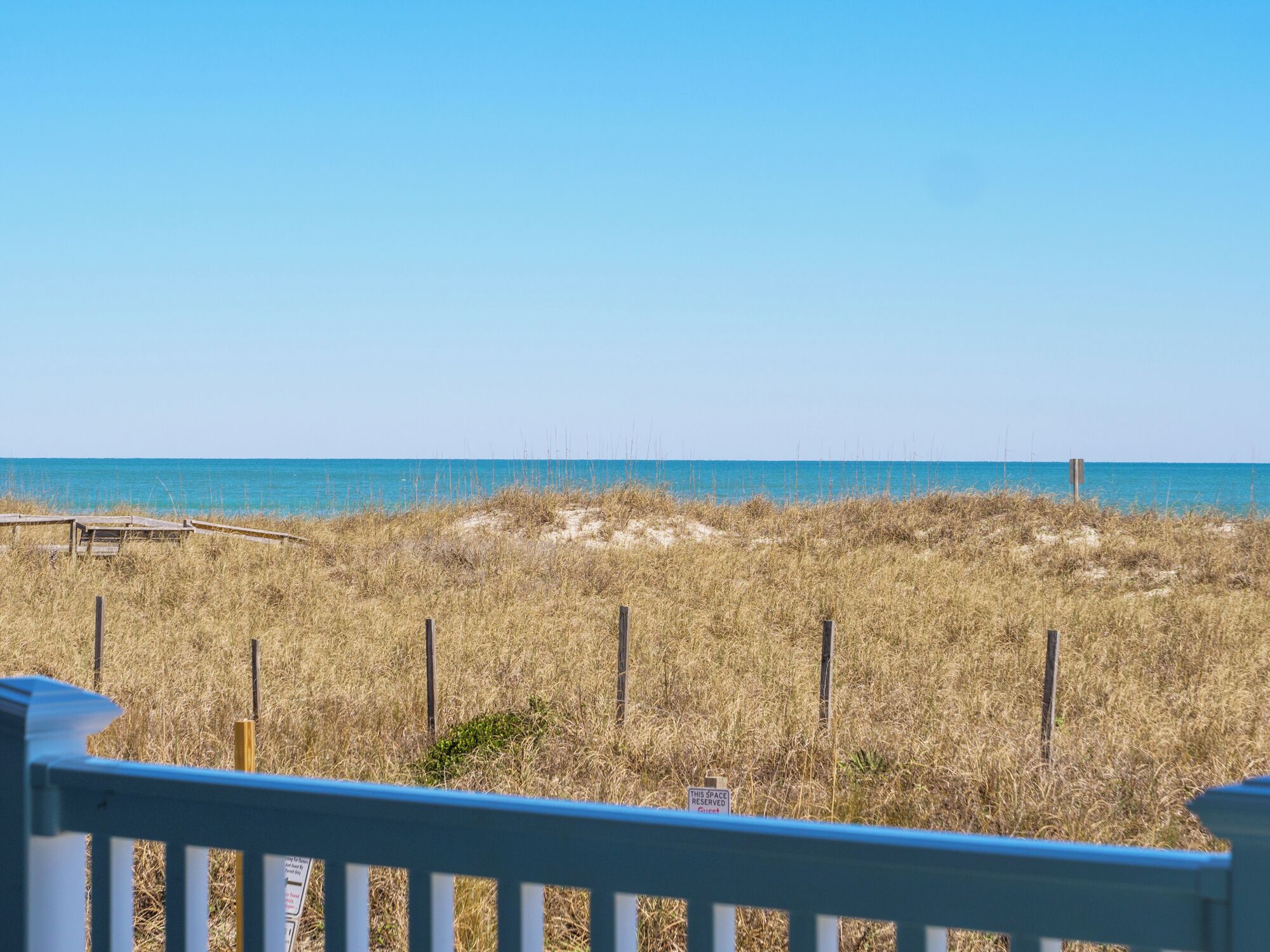 A beach view with a wooden fence and a sign indicating a guest area.