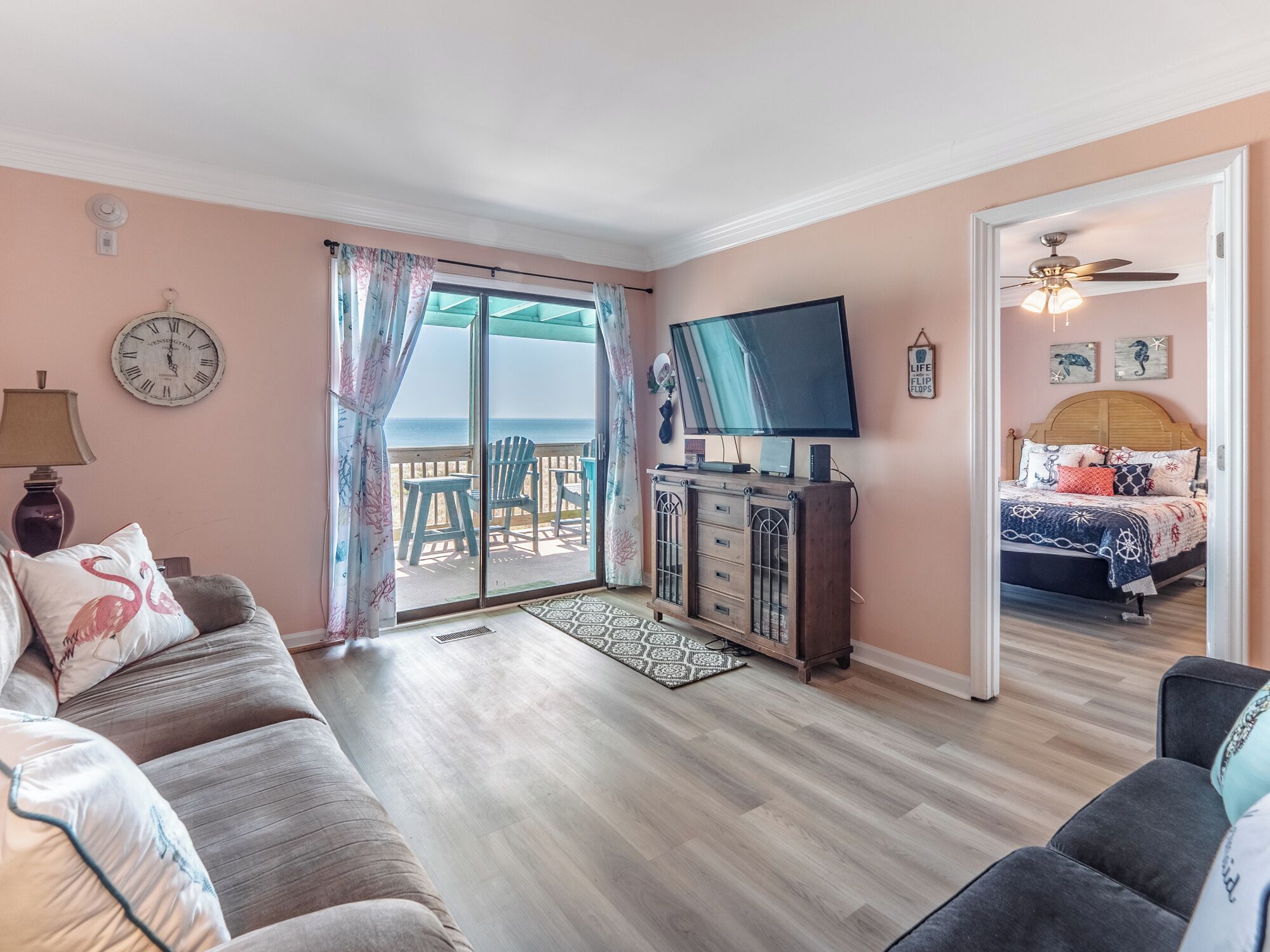 A room with a large window, a flat-screen TV, a sofa, a bed, and a wooden cabinet.