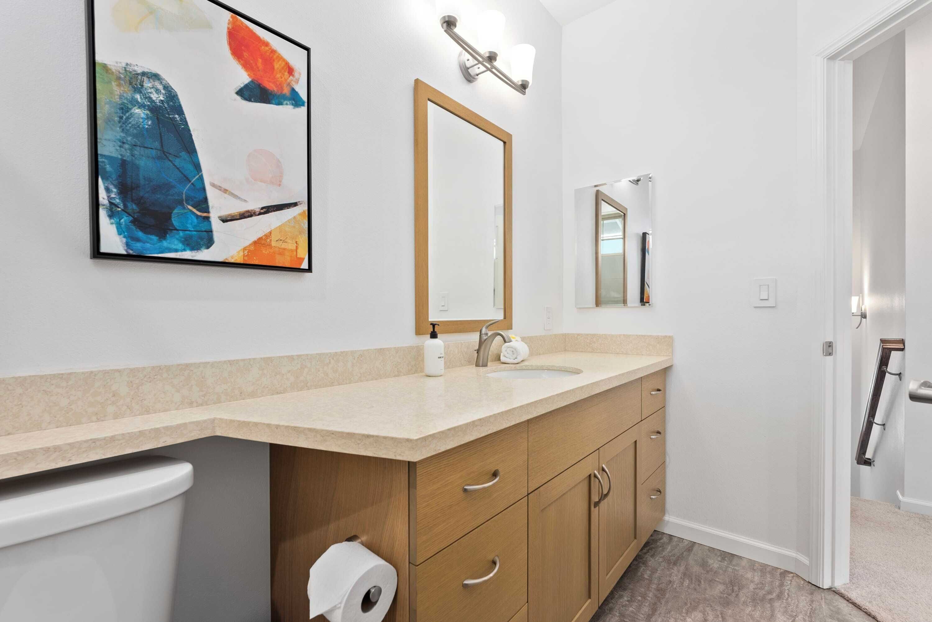 Un bagno moderno con un piano d'appoggio beige, mobili in legno, uno specchio grande e un water.