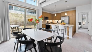 A modern kitchen with wooden cabinets, a central island, and a dining area with a white table and black chairs. - @marbella Lane - Elegant 3BR w/ Marvelous Views (Waianae)
