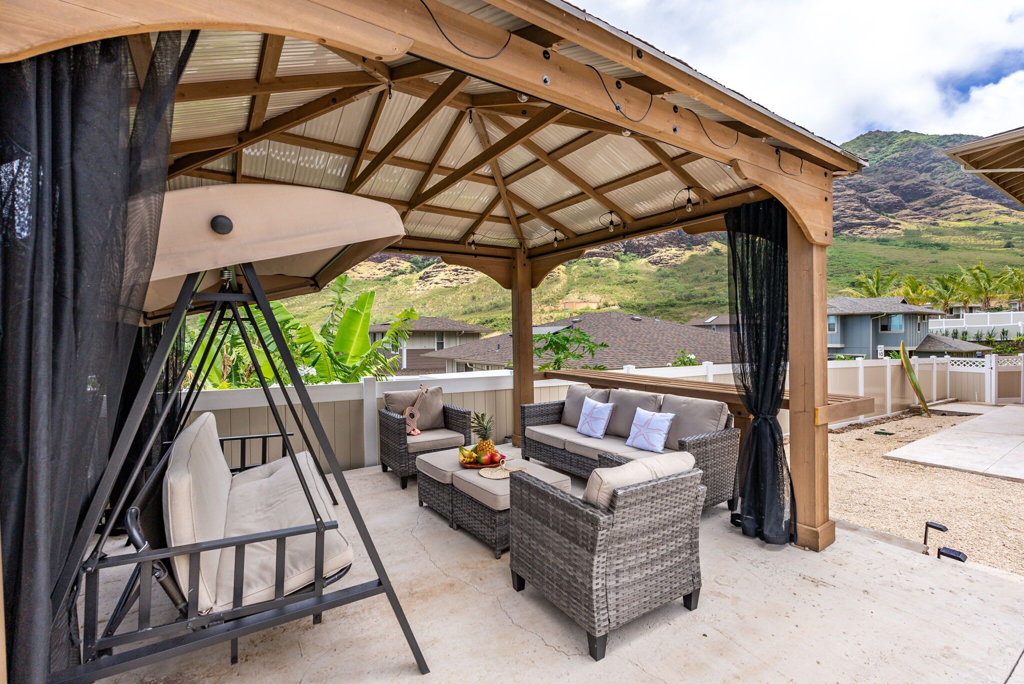 An outdoor patio with wicker furniture, a swing, and a covered area with a view of mountains.