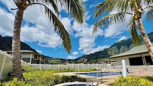 A hot tub surrounded by lush greenery and palm trees, with a pool and a view of mountains in the background. - @ Marbella Lane - Stunning Gem w/ MT & Ocean Views (Waianae)