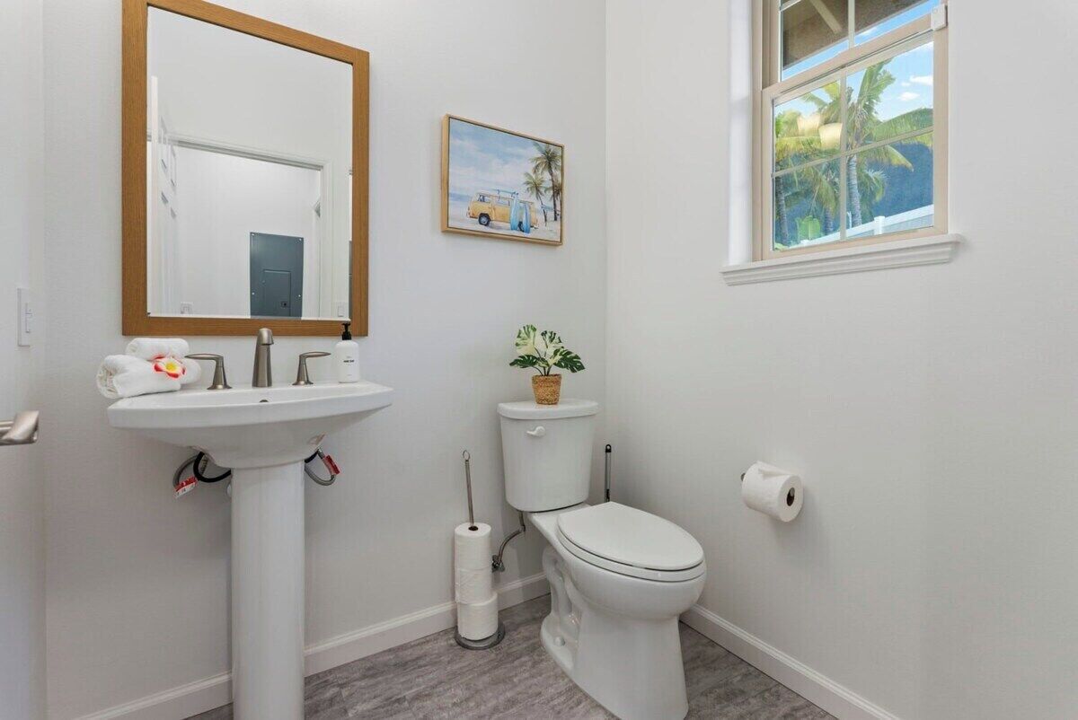 Un baño con lavamanos, inodoro y ventana con vista a palmeras.