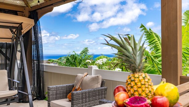 A patio with wicker furniture, a guitar, and a fruit bowl with pineapple, apple, and dragon fruit. - @ Marbella Lane - Stunning Gem w/ MT & Ocean Views (Waianae)