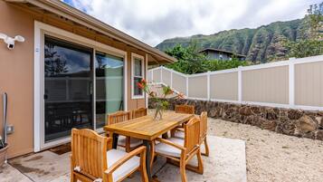 A wooden table and chairs set outside a house with a stone wall and a view of a mountain.
