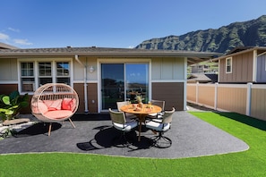 Ein Haus mit Terrasse, das einen runden Tisch, Stühle, einen Hängesessel und einen Blick auf einen Berg bietet.