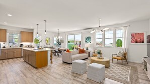 A spacious kitchen with wooden cabinets, a dining area with a table and chairs, and a living room with a sofa and ottomans. - @ ML Aloha Hoonani 3BR Home MT & Ocean Views! (Waianae)