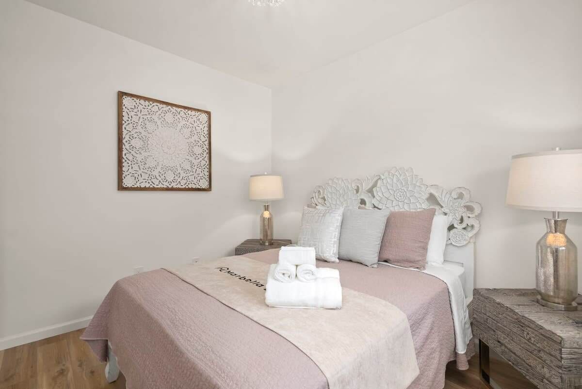A neatly made bed with a pink blanket, a decorative headboard, and a wall-mounted artwork.